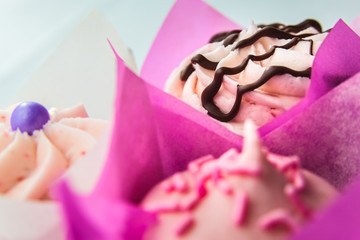 Three Cupcakes In Pink Wrappers Against A White Background
