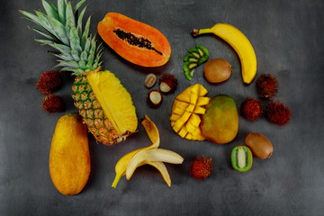 Tropical fruits assortment on a dark wood background with top view.
