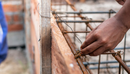 A worker using steel wire and pincers to secure steel bars, preparing for concrete pouring on indutrial construction site