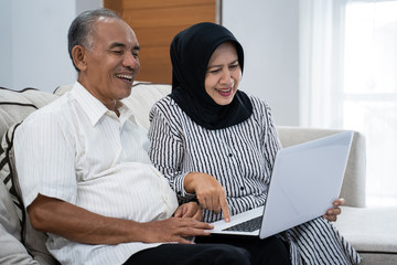asian mature couple enjoying a modern technology watching a news by a laptop
