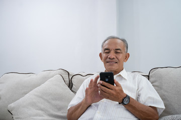 asian senior old man using smartphone while relaxing in livingroom at home