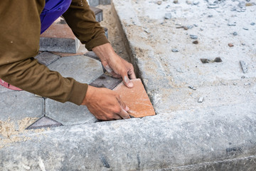 Close-up of hands of worker working on placing stone block for foot path.
