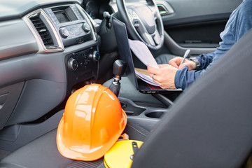 Young engineer working with laptop inside car. Helmet place on car seat.