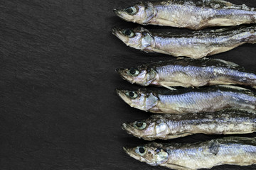 Dry small European smelt fishes on black stone background with copy space