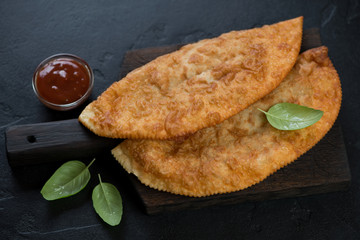 Black wooden serving board with deep-fried turnovers chebureki, studio shot on a black stone surface