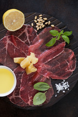 Closeup of carpaccio made of raw marbled beef with parmesan, lemon, pine nuts, olive oil, salt and fresh green basil, flatlay