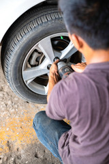A man is using a remover tool to remove a wheel of that white car