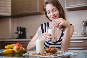 Woman drinking organic almond milk holding a glass in her hand in the kitchen. Diet healthy...