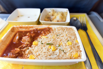 Tray with delicious food on the plane, economy class travel. Tasty meal served in the aircraft interior. Sun shining through the airplane window.