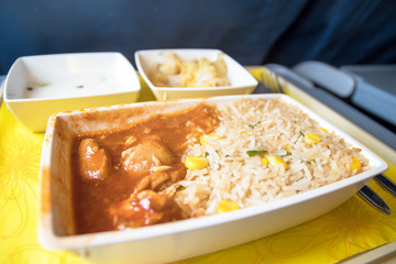 Tray with delicious food on the plane, economy class travel. Tasty meal served in the aircraft interior. Sun shining through the airplane window.