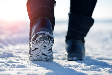 Female feet in winter boots, walking in the snow.