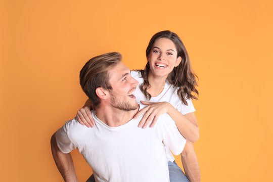 Image of caucasian couple looking at each other and smilling while sitting on back of content man isolated over yellow background.
