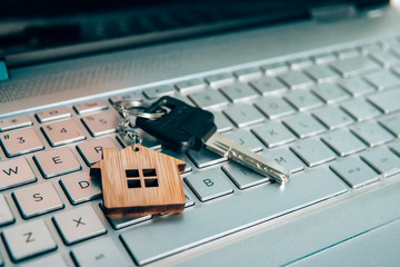 Metallic key on key ring with house symbol lying on laptop keyboard. Real estate and internet...