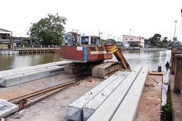 An excavator loader machine and concrete piles on pontoon floating in river for riverside construction work