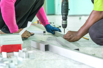 Two Workers work on screw drilling on aluminium profile with electric drill.