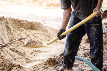 A worker use the shovel to fill the sand into the wheelborrow for construction of new house....