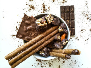 Chocolate bars, chocolates, chocolate tubes sprinkled with cocoa in a white bowl with.