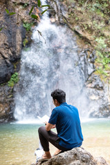 Obraz premium Young man sit and turn back reading book at waterfall.