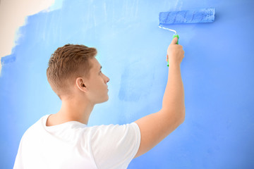 Male painter using roller for refurbishing color of wall indoors