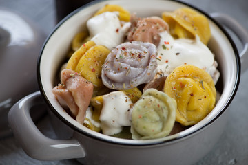 Close-up of a pot with boiled colored dumplings pelmeni and sour cream, studio shot