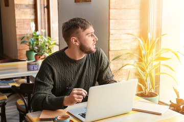 Young freelancer with laptop working in cafe