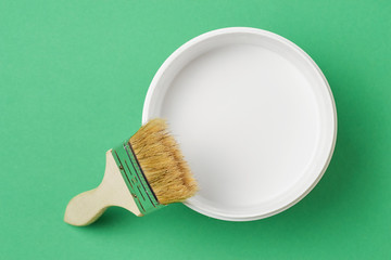 Brush and paint can with white color on a green background, top view