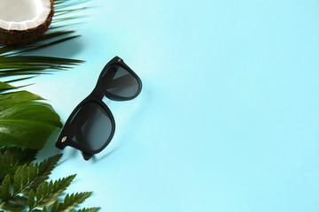 Stylish sunglasses with tropical leaves on color background