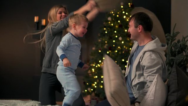 Happy parents with their son playing sitting on the bed in pajamas at Christmas A pillow fight at Christmas before the new year