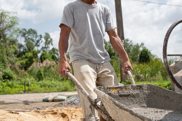 Construction worker pull wheelbarrow. Ready cement in wheelbarrow. Cement mixer machine equipment...