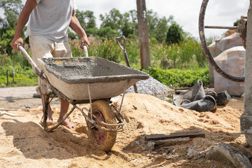 Construction worker pull wheelbarrow. Ready cement in wheelbarrow. Cement mixer machine equipment...