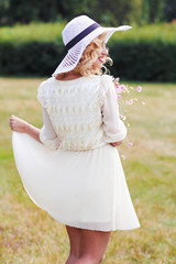 Curly blonde in a white hat walks in a park with a bouquet of field violet flowers..