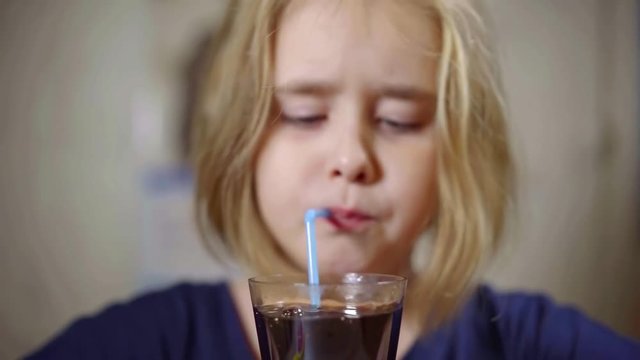 Close-up shot of a cute little girl with drinking coke from a glass.