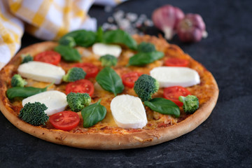 Italian pizza with Mozzarella cheese, tomatoes, broccoli, Spices and fresh basil. Pizza and kitchen napkin near, on black stone background