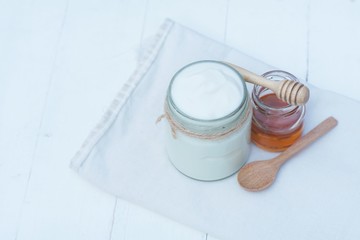 Plain yoghurt in white bowl, honey, cereal, raisin and wood spoon on white wooden table background
