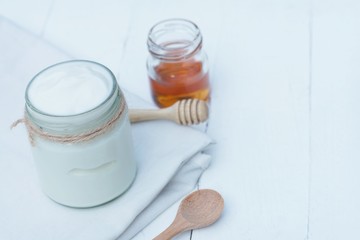 Plain yoghurt in white bowl, honey, cereal, raisin and wood spoon on white wooden table background