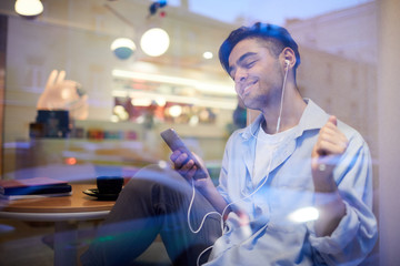 Young handsome man with smartphone and earbuds relaxing in cafe and enjoying his favorite music