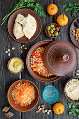 Moroccan traditional tajin and various snacks on dark wooden table. Carrot Salad, Couscous, Olives, Hummus. Flat lay