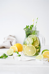 Lemonade in a glass jug on light background. Lemon, Mint, Lime and Ice Ingredients