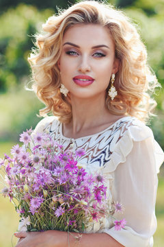 Curly blonde in a park with a bouquet of field violet flowers..