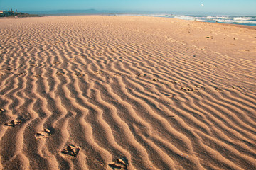 Close up of a wavy, ondulated sandy beach; golden light and sand, nobody around