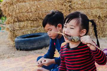 Little girl eating fried fish on the field looking happiness by the boy staying beside