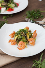 Salad with shrimps on a white plate is on the table.