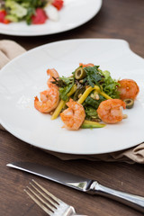 Salad with shrimps and greens on a white plate is on the table.