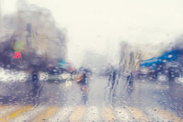 Blurred view through the windshield of a car with raindrops at a crossroad and pedestrian crossing.