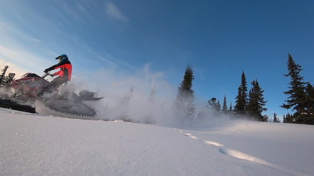 beautiful snowmobile jump. boondocking, blue sky. snowmobile with splashes of snow and whirlwinds. bottom and side view. bright snowmobile in the mountain forest.  stock video footage. Slow motion