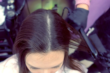 Hairdresser straights dark brown hair of beautiful woman using hair tongs in beauty salon. Top view.