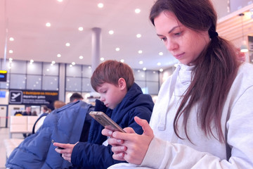 Woman with her son browsing on mobile phones in airport hall waiting for flight.