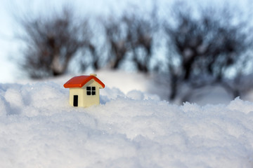 toy house on a snowdrift on the background of bushes