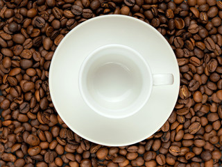 Coffee beans as a background and a white cup on a saucer