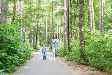 Family, summer and nature concept - Attractive young woman and beautiful little daughter girl walking in green park